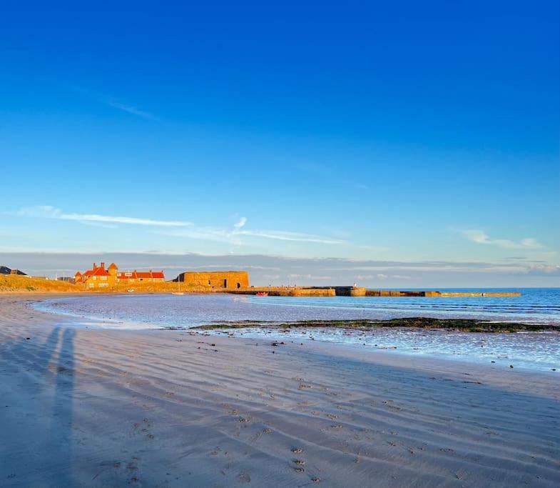 a beach with buildings in the distance and the ocean at Rockview Beadnell - Perfect Family Retreat in Beadnell