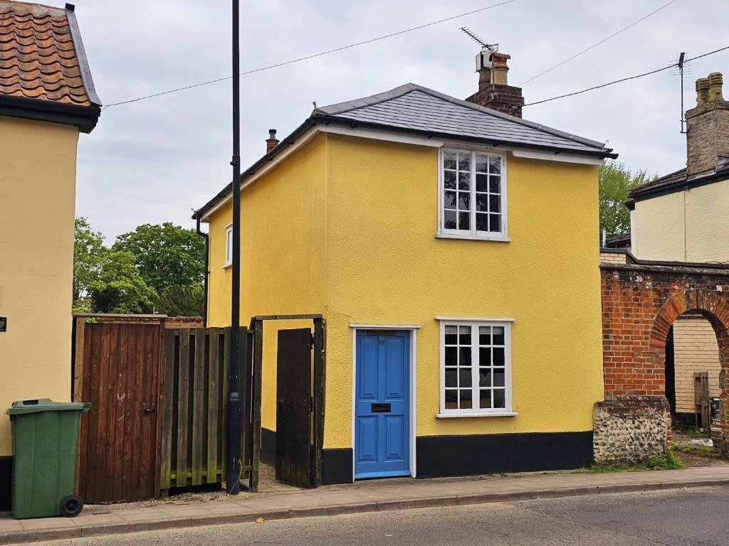 una casa amarilla con una puerta azul en una calle en Perfectly Located Pretty Cottage, en Diss