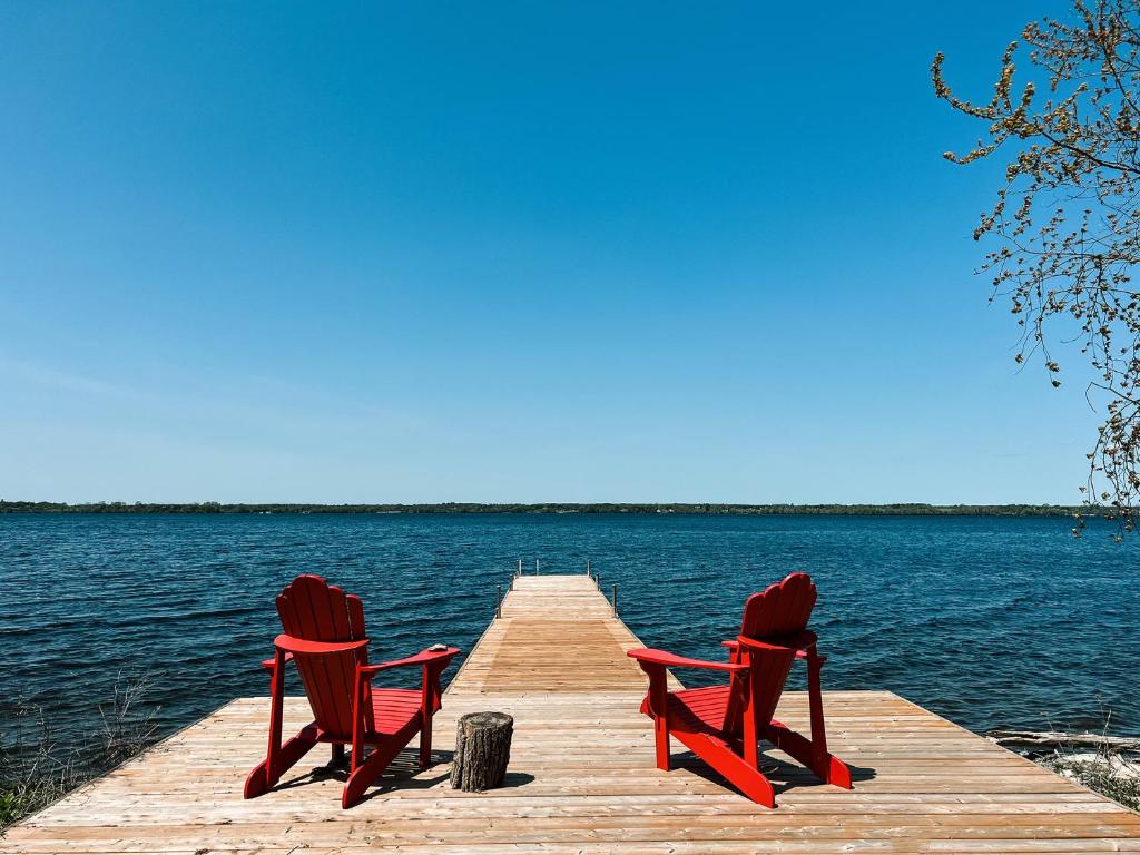 two red chairs sitting on a dock on a lake at Tanglewood - Large Waterfront Home in PEC in Waupoos