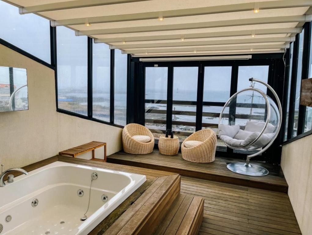 a bathroom with a tub and a chair and windows at Farms Village in Jeju