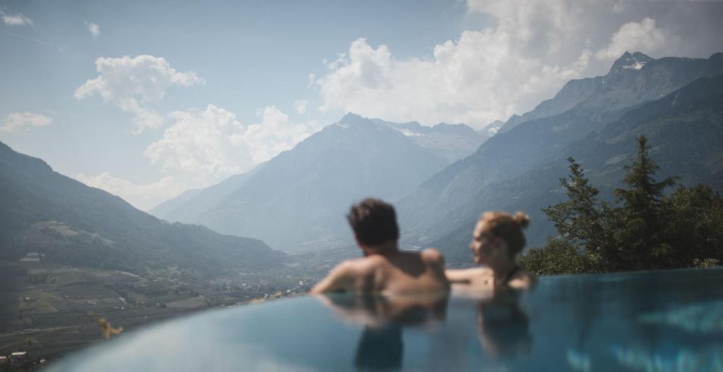 a man and a woman standing in a swimming pool overlooking mountains at Hotel Sonnbichl in Tirolo