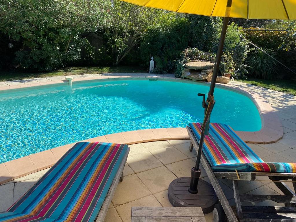 uma piscina com duas espreguiçadeiras e um guarda-sol em Studio bord de piscine em Sérignan-du-Comtat