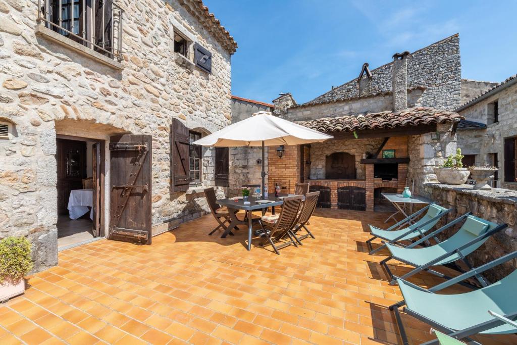 eine Terrasse mit einem Tisch, Stühlen und einem Sonnenschirm in der Unterkunft La Médiévale - Charmante maison de caractère in Ruoms