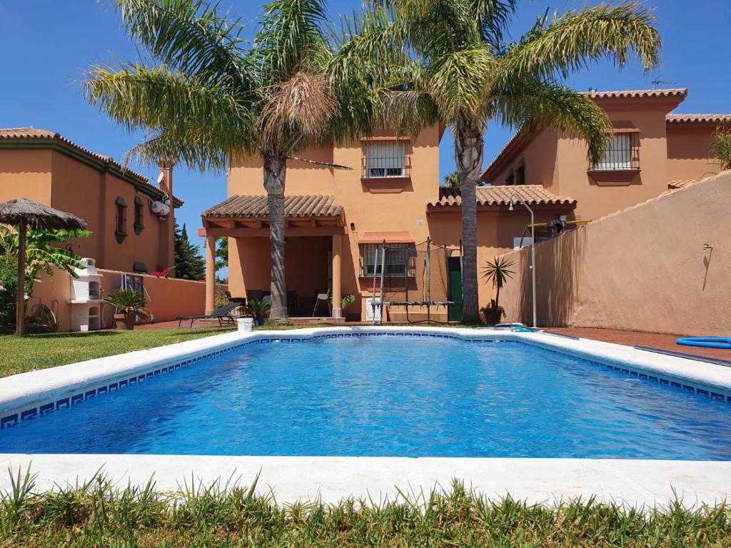 a swimming pool in front of a house with palm trees at Villa Ostrero in Chiclana de la Frontera