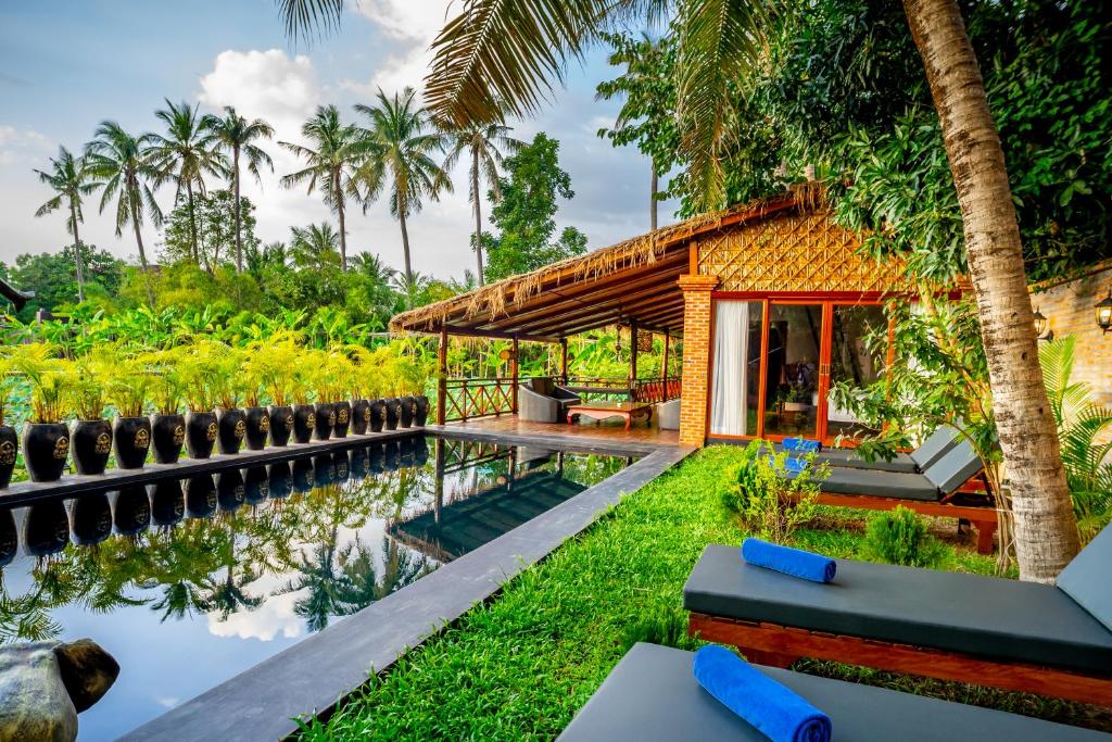 a house by the water with palm trees at Authentic Khmer Village Resort in Siem Reap