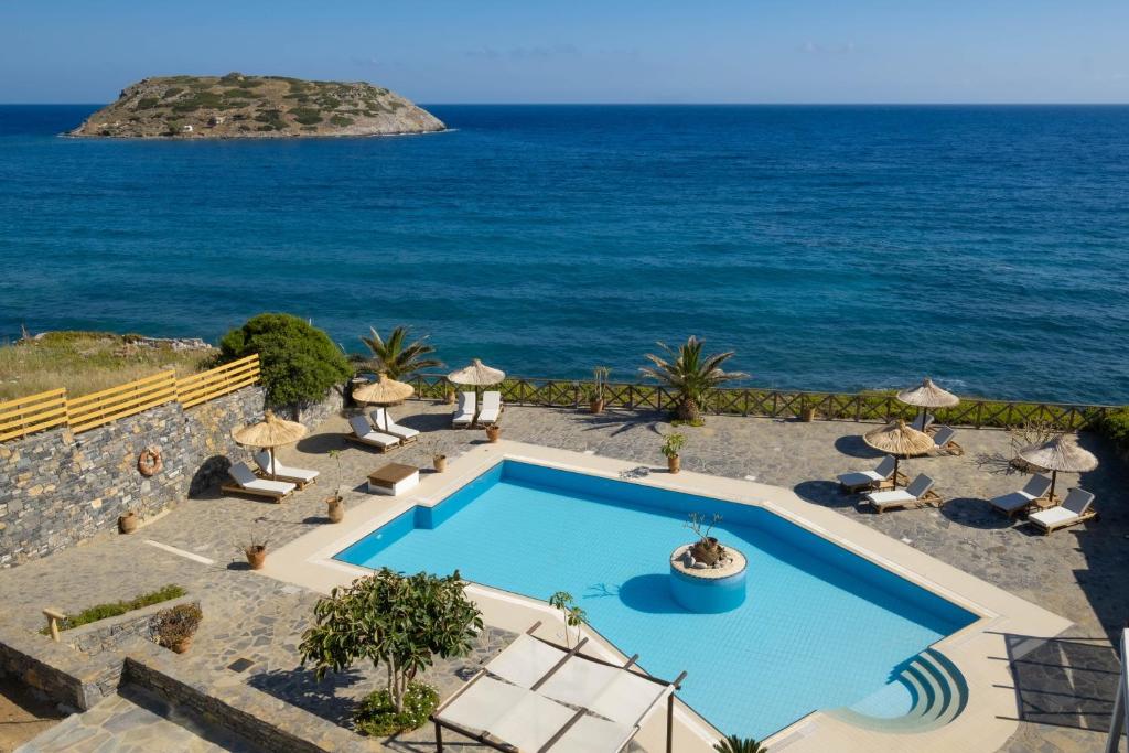 a swimming pool with chairs and the ocean in the background at Mochlos Blue in Mochlos