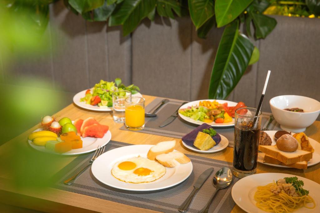 A plated breakfast spread with fruit, eggs, noodles, bread and drinks.