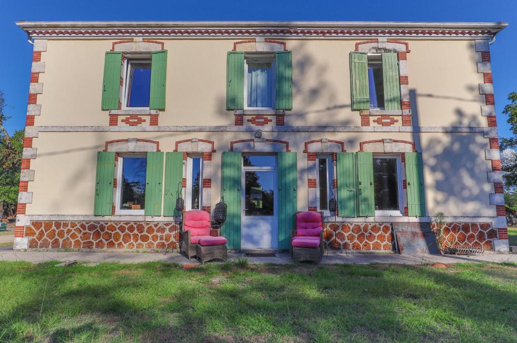an old house with green shutters and pink chairs at Domaine les Maisons des Houssats in Trensacq
