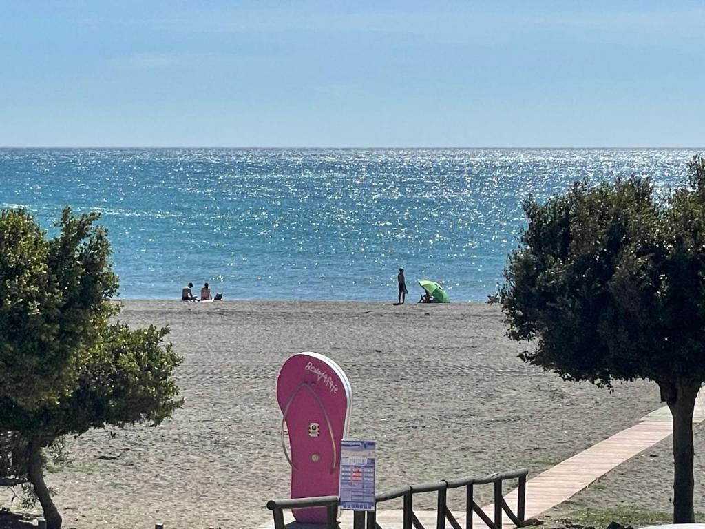 una tabla de surf rosa en la playa con gente en el agua en Casa Julia Apartamento Playa Benajarafe, en Vélez-Málaga