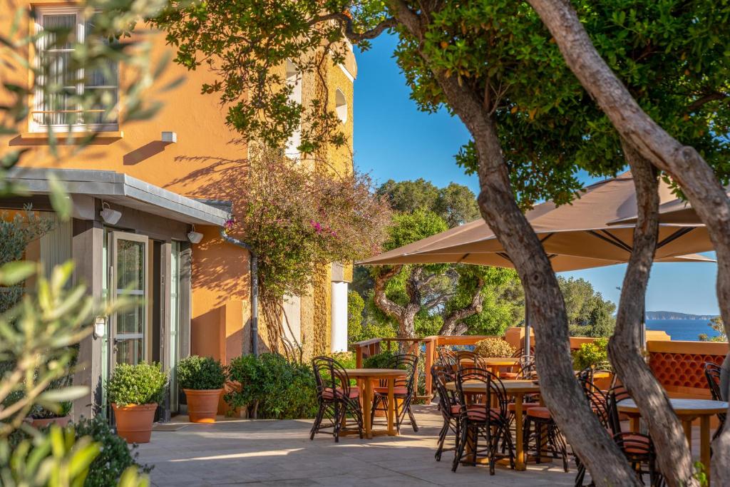 a patio with tables and chairs under an umbrella at Les Terrasses du Bailli in Rayol-Canadel-sur-Mer