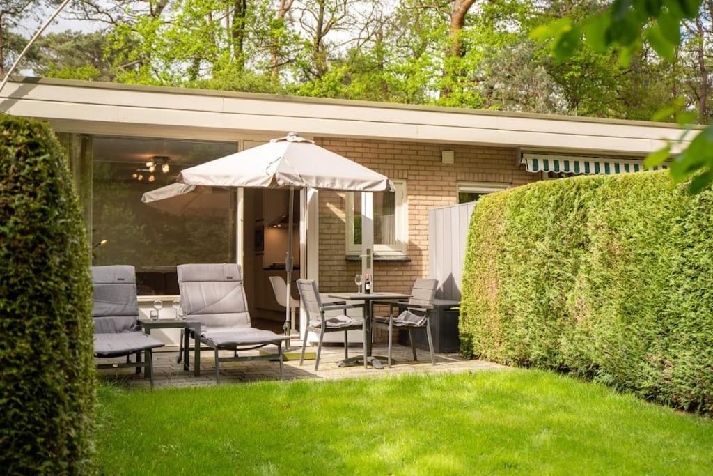 a patio with a table and chairs and an umbrella at Heerlijk vakantiehuisje op rustig Natuurpark in Otterlo