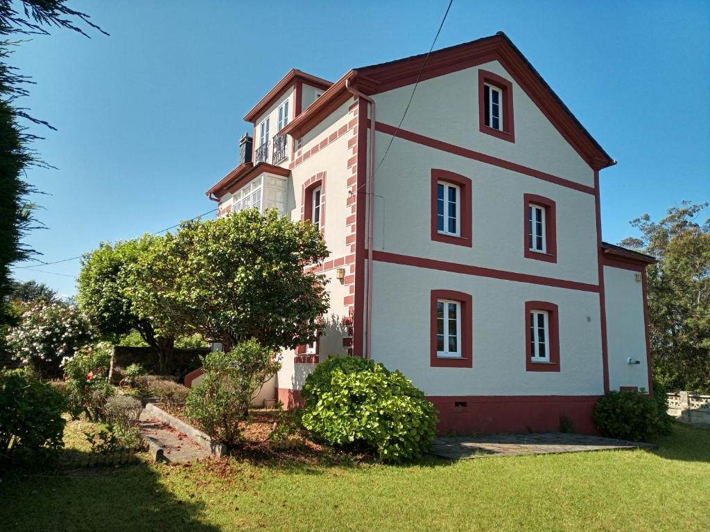 uma grande casa branca com acabamento vermelho num quintal em Casa Tula em Ortigueira