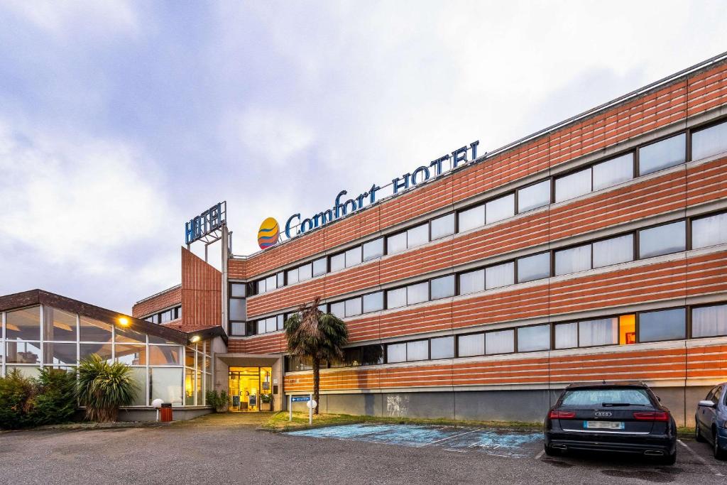 un bâtiment avec une voiture garée devant lui dans l'établissement Comfort Hotel Toulouse Sud, à Ramonville-Saint-Agne