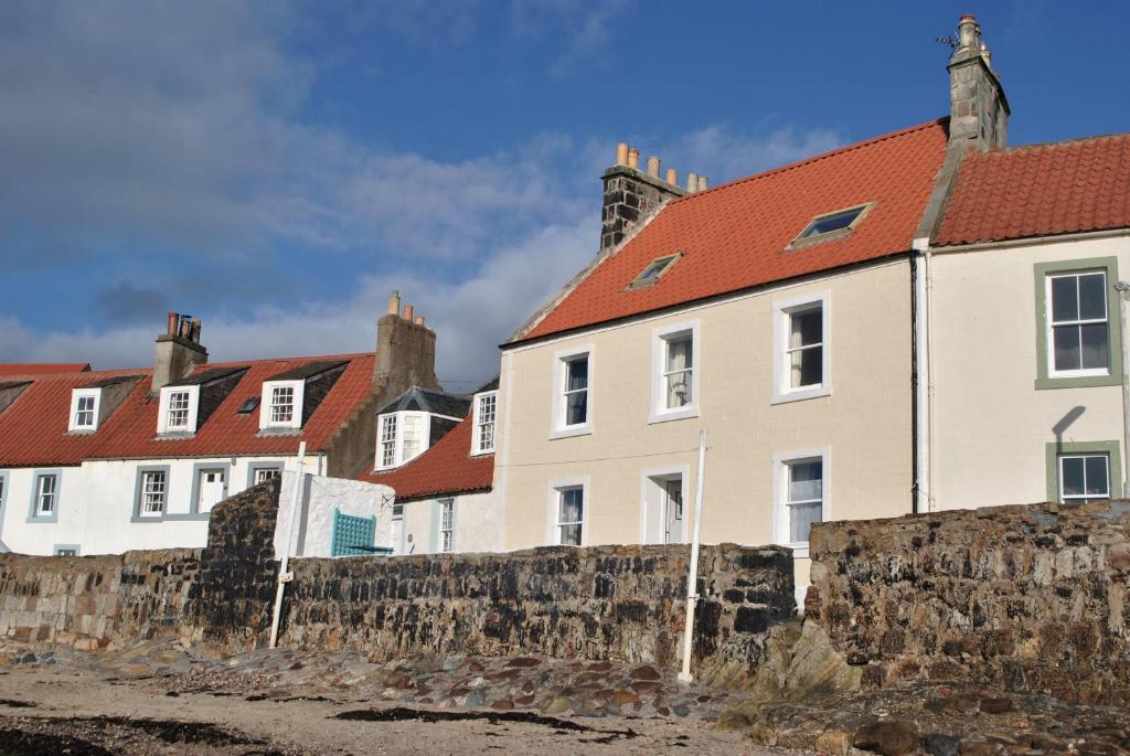 uma fila de casas com telhados vermelhos atrás de uma parede de pedra em Westshore House- fabulous waterfront home Fife em Pittenweem