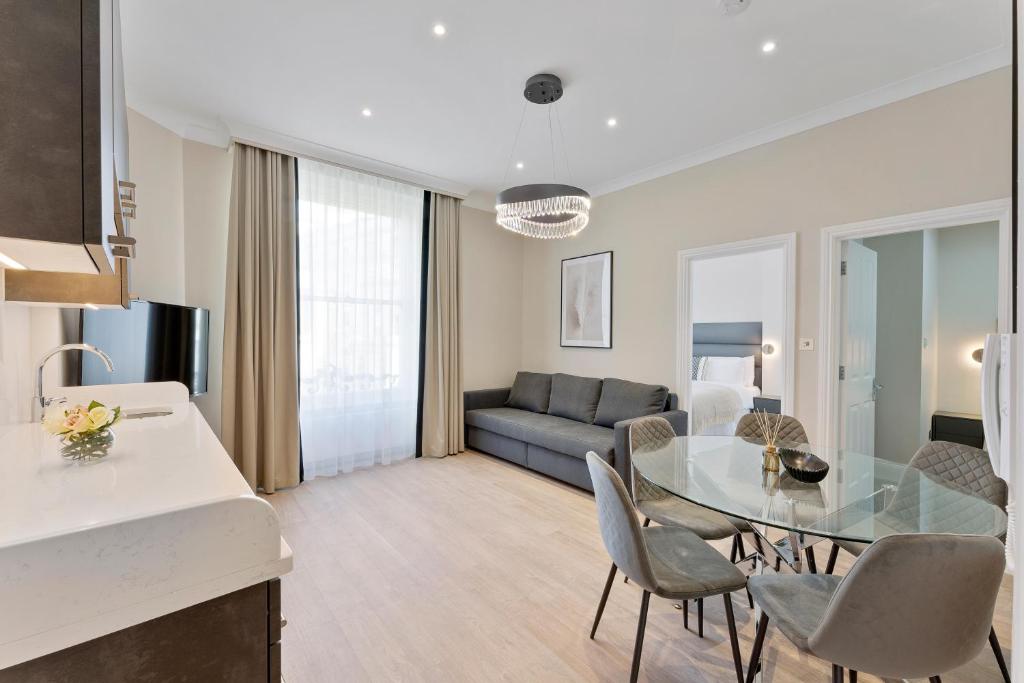 cocina y sala de estar con mesa de cristal y sillas en Cleveland Residences Paddington, en Londres