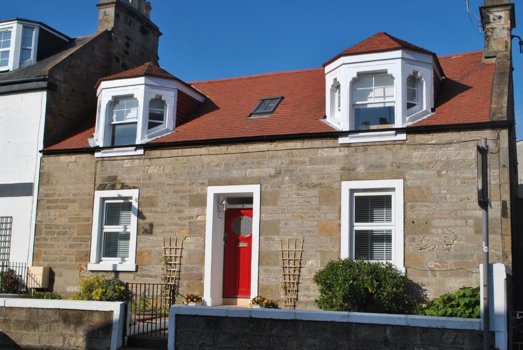 a brick house with a red door at Craws Nest Cottage- stylish traditional home in Pittenweem