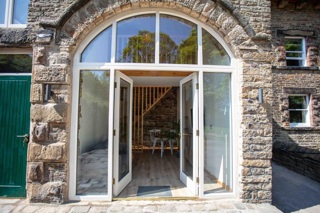 uma porta arqueada para uma casa de pedra com portas de vidro em Stunning stone coach house em Marple