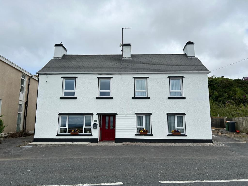 a white house with a red door on a street at Mary's of Mulranny in Mulranny
