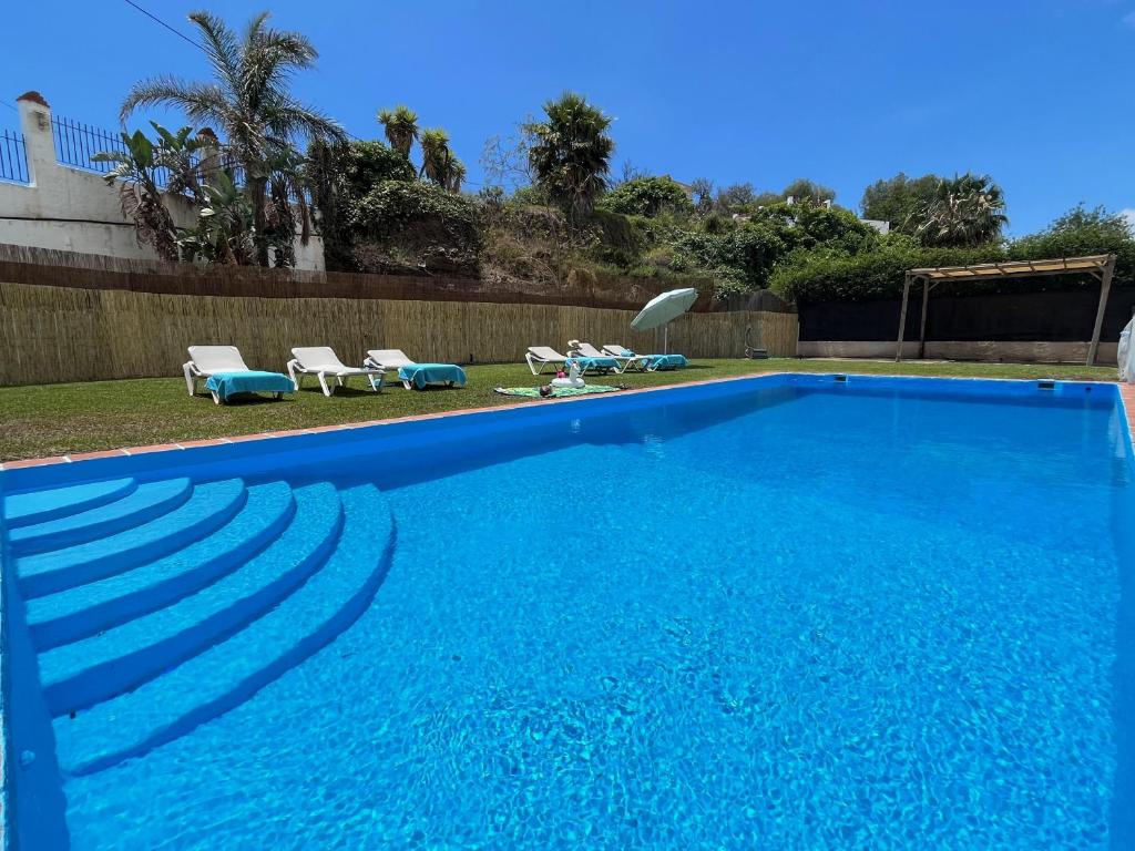 a large blue swimming pool with lounge chairs in a yard at Nerja Paradise Rentals - Villa Alminares in Nerja