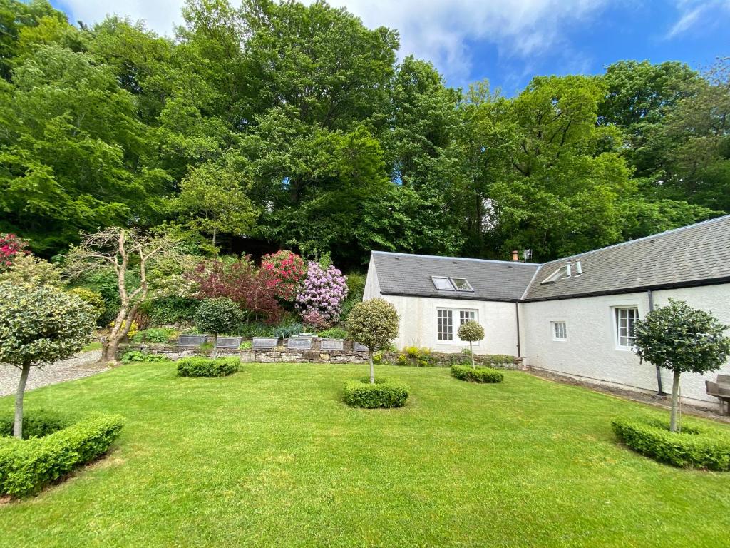 a yard with a white house and trees at Spacious cottage - walk to Crieff in Crieff