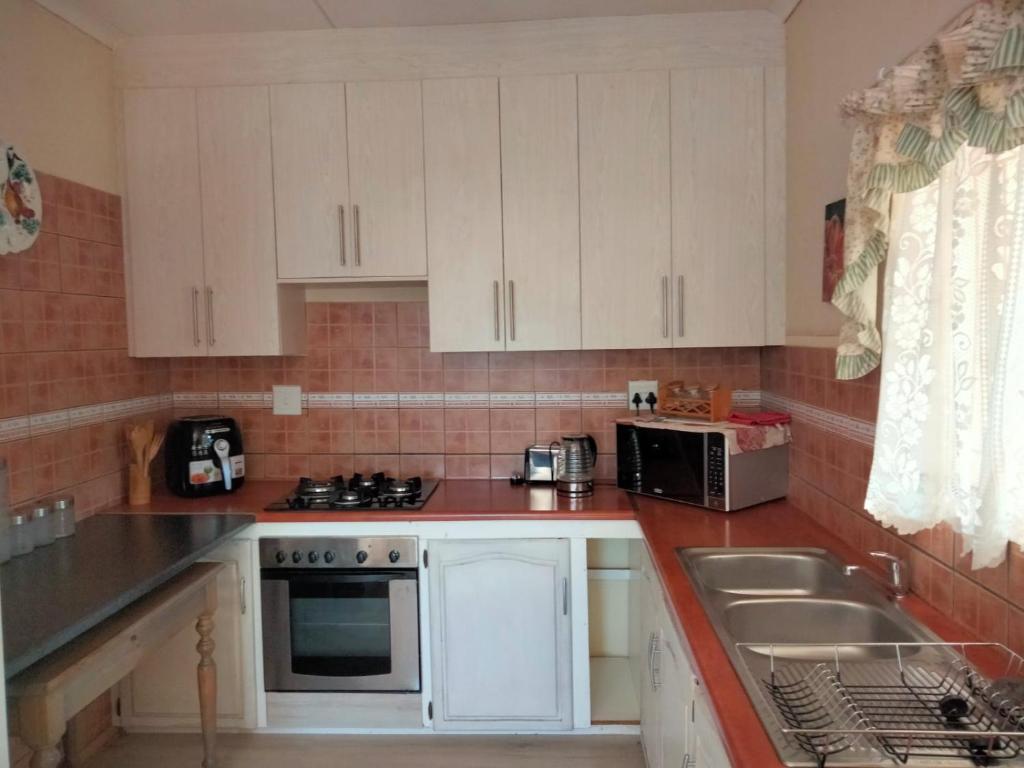 een kleine keuken met witte kasten en een wastafel bij At Home Apartments in Mokopane