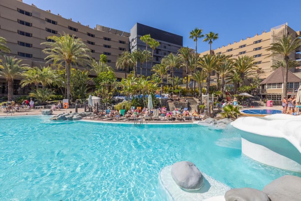 una piscina en un complejo con gente sentada en sillas en Abora Continental by Lopesan Hotels, en Playa del Inglés