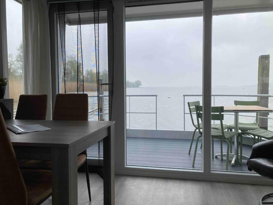 uma sala de estar com uma mesa e vista para uma varanda em Houseboot Cormorant, lake view em Biddinghuizen