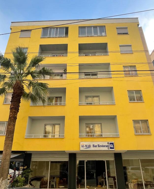a yellow building with a palm tree in front of it at Almar Apartments in Durrës