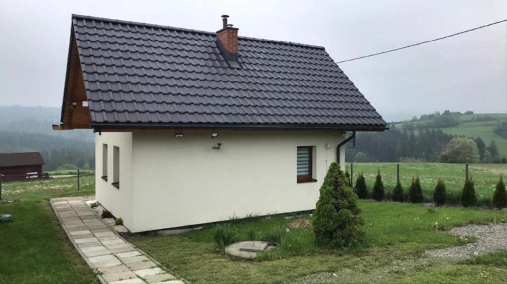 a white house with a black roof in a field at Domek do wynajęcia SkoSki in Jaworzynka