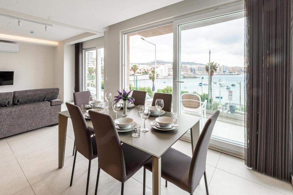 een eetkamer met een tafel en stoelen en een groot raam bij Seafront Luxury Apartment in St Paul's Bay