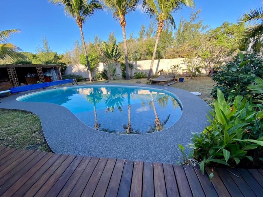 una piscina con palmeras y una terraza de madera en Très belle villa,piscine chauffée, jacuzzi,hammam. en Étang-Salé les Bains