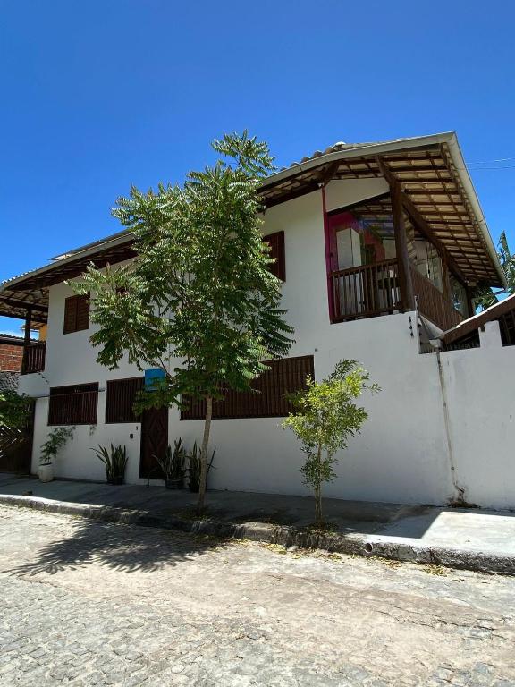 a white house with a tree in front of it at Kitnet próximo à Praia do Forte in Mata de Sao Joao