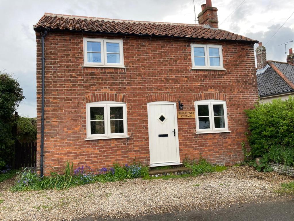 a brick house with a white door and two windows at Wallflower Cottage in Norwich