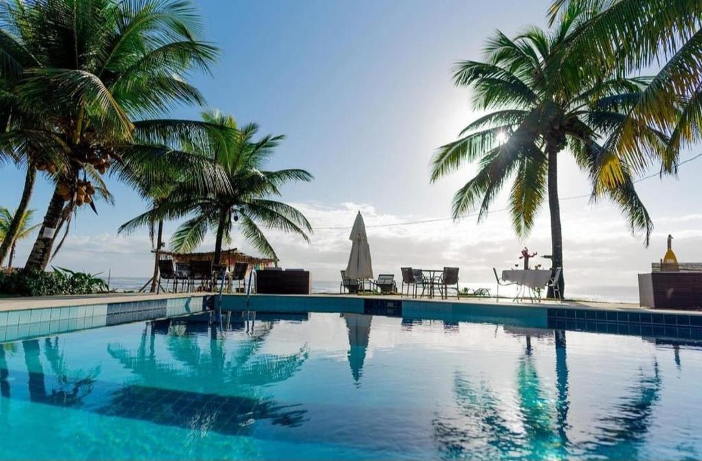 a swimming pool with palm trees and the ocean at Eden One in Ilhéus