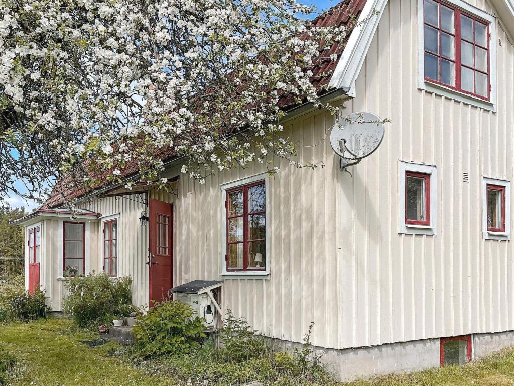 una casa blanca con una puerta roja y un árbol florido en Holiday home LIDKÖPING X, en Tallbacken