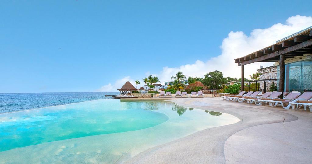 una grande piscina con sedie e l'oceano di Grand Park Royal Cozumel - All Inclusive a Cozumel