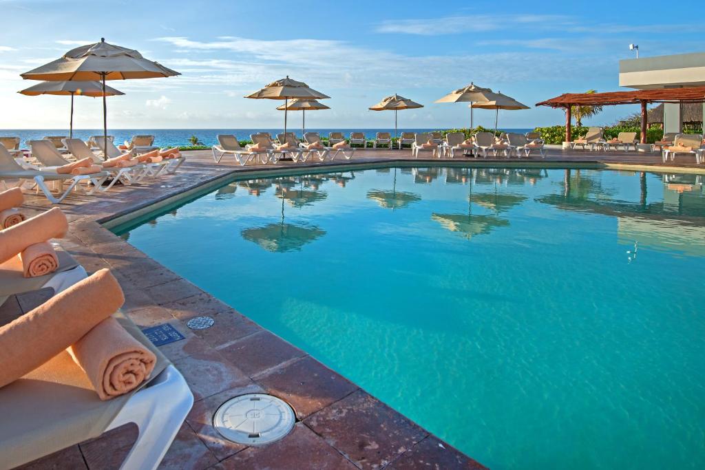a swimming pool with chairs and umbrellas and the ocean at Park Royal Beach Cancun - All Inclusive in Cancún