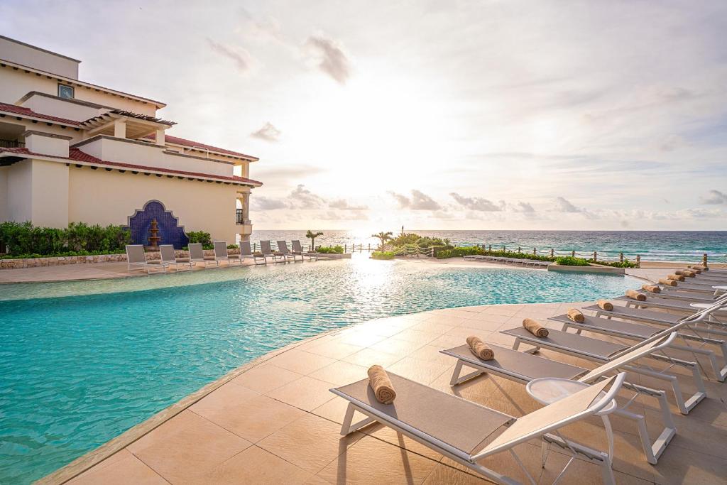 Grand Park Royal Cancun - All Inclusive في كانكون: حمام سباحة مع الكراسي والمحيط في الخلفية