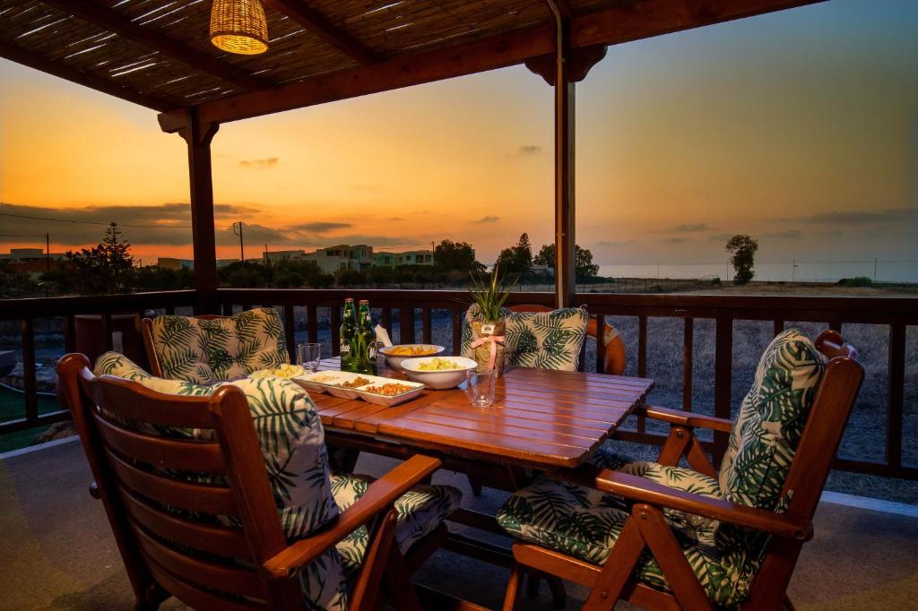 - une table et des chaises en bois sur une terrasse avec vue sur le coucher du soleil dans l'établissement Mayia Sunset sea front house Gouves Heraklion, à Gouves