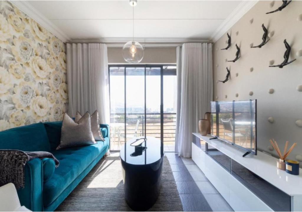 uma sala de estar com um sofá azul e uma grande janela em The Steynview Apartment - Fourways Sandton em Joanesburgo