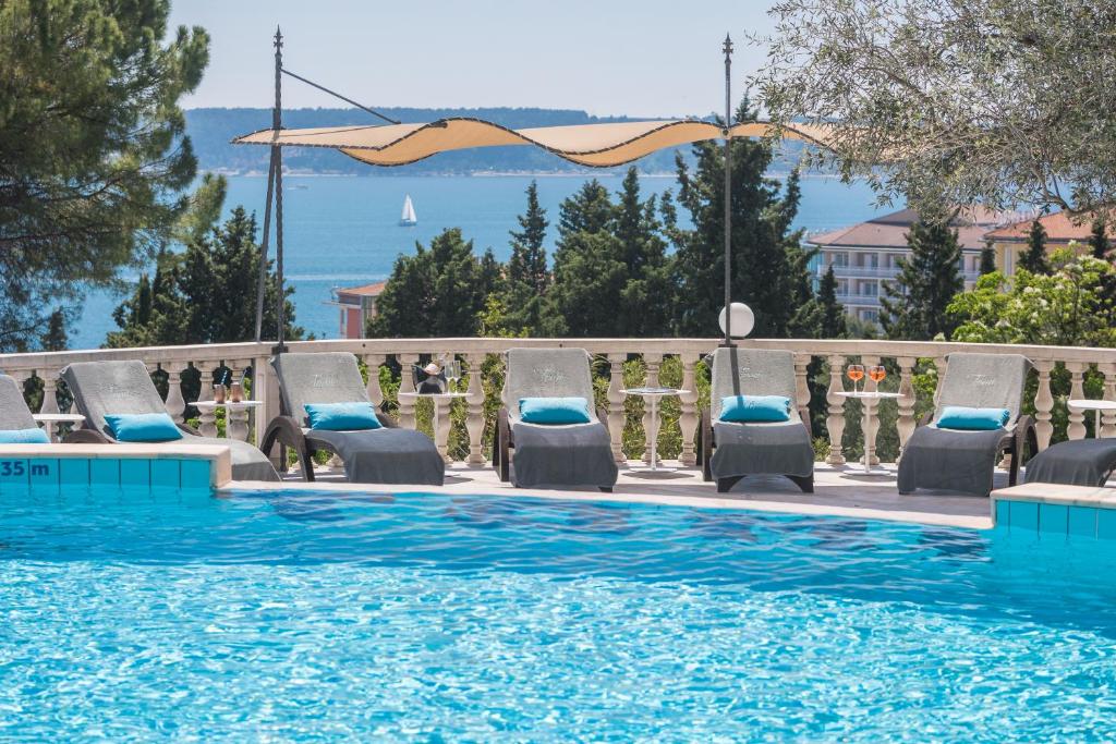 a swimming pool with chaise lounge chairs and the ocean at Hotel Tomi in Portorož