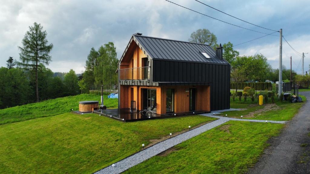 dom z czarnym dachem na zielonym polu w obiekcie Wood Lake Rożnów w mieście Rożnów