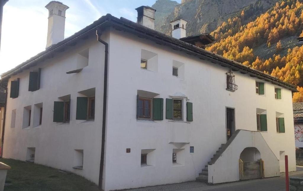 a white building with green windows and a mountain at Posta Veglia in Sils Baselgia