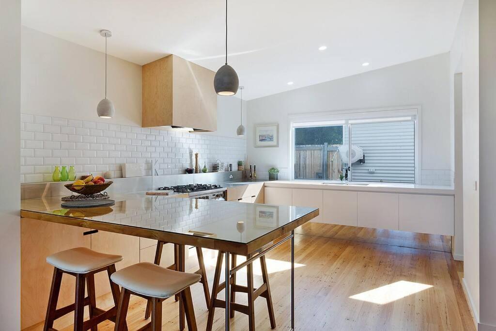 una cocina blanca con mesa y taburetes. en Sea Change and Studio on Tasman, en Merimbula