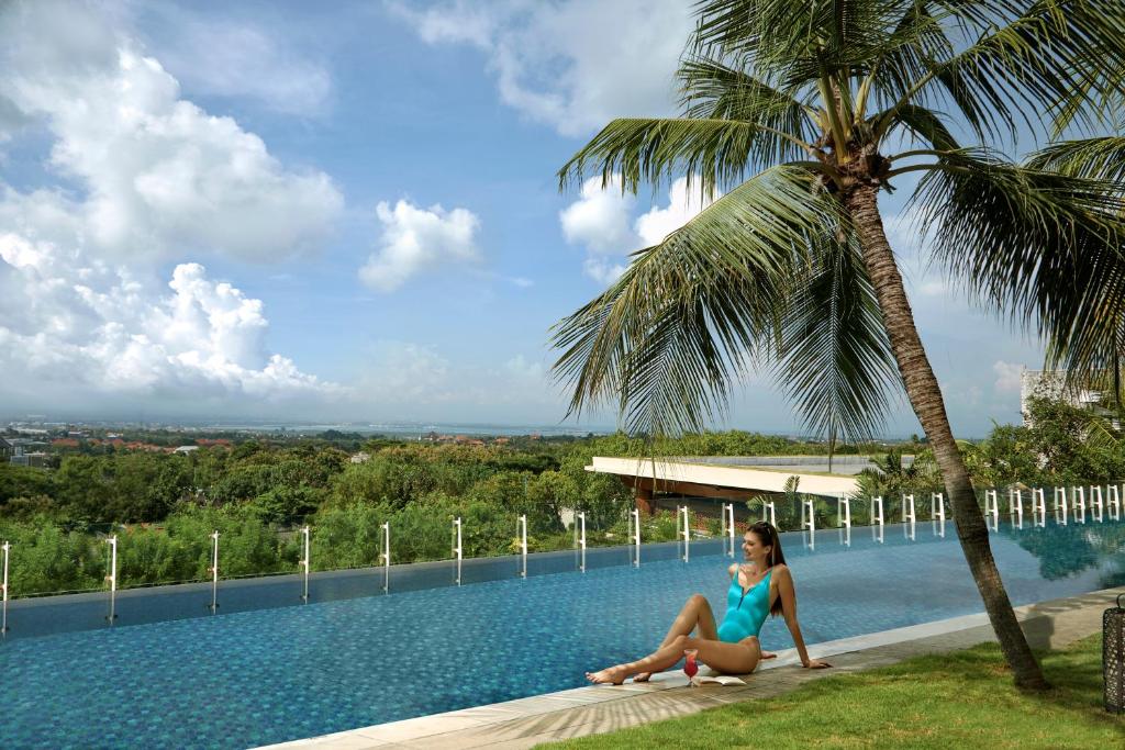 une femme assise sous un palmier à côté d'une piscine dans l'établissement Four Points by Sheraton Bali, Ungasan, à Jimbaran