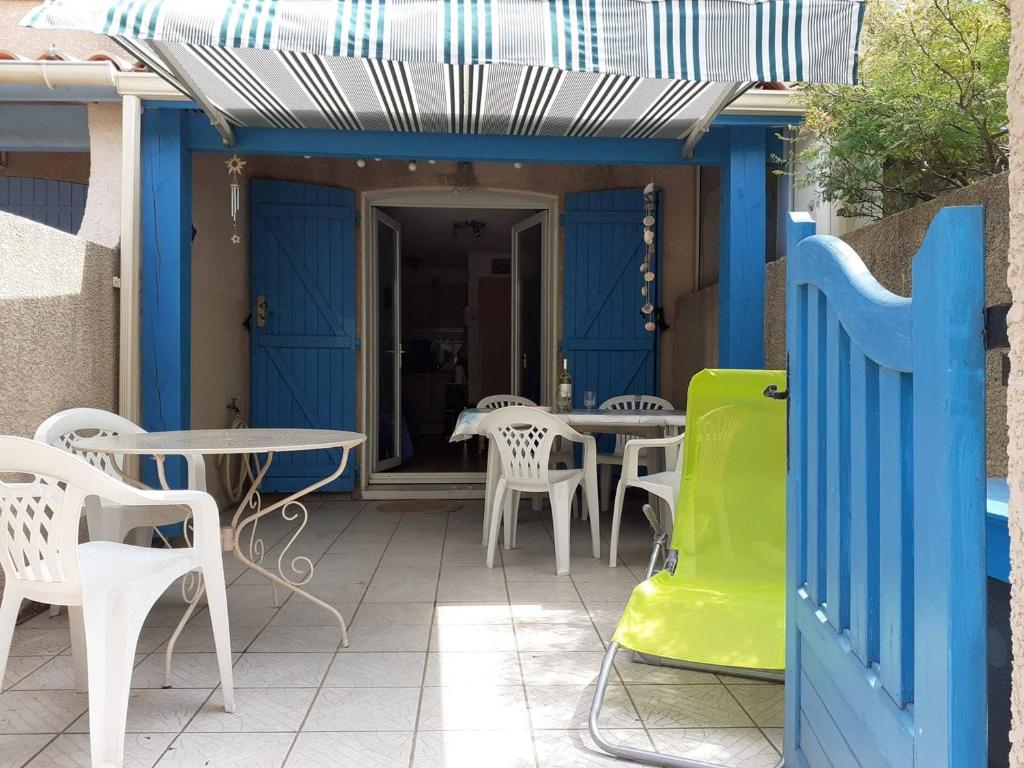 d'une terrasse avec des tables et des chaises blanches et une porte bleue. dans l'établissement Maison climatisée 3 pièces, 6 couchages près de la plage du Grazel à Gruissan - FR-1-229-851, à Gruissan