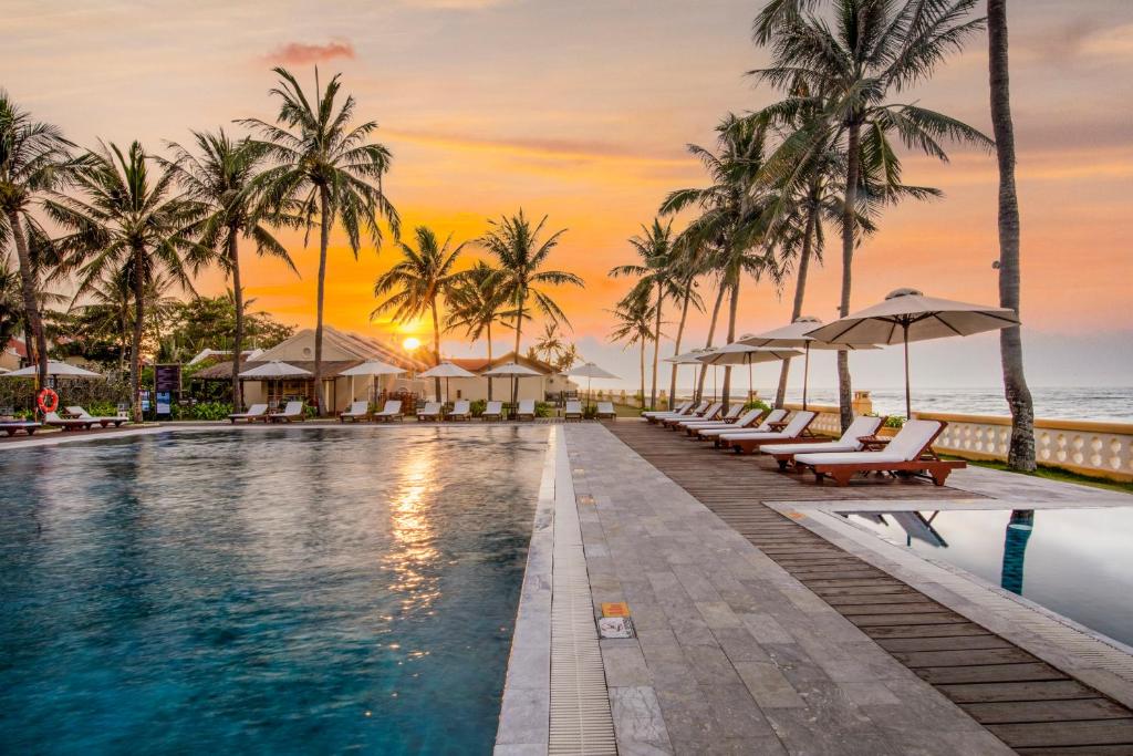 uma piscina num resort com palmeiras e o oceano em Victoria Hoi An Beach Resort & Spa em Hoi An