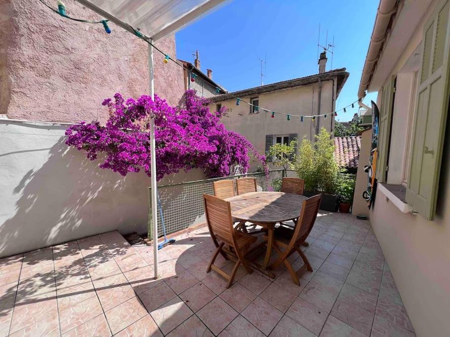 een tafel en stoelen op een patio met paarse bloemen bij Maison dans les rues piétonnes du vieux Hyères in Hyères