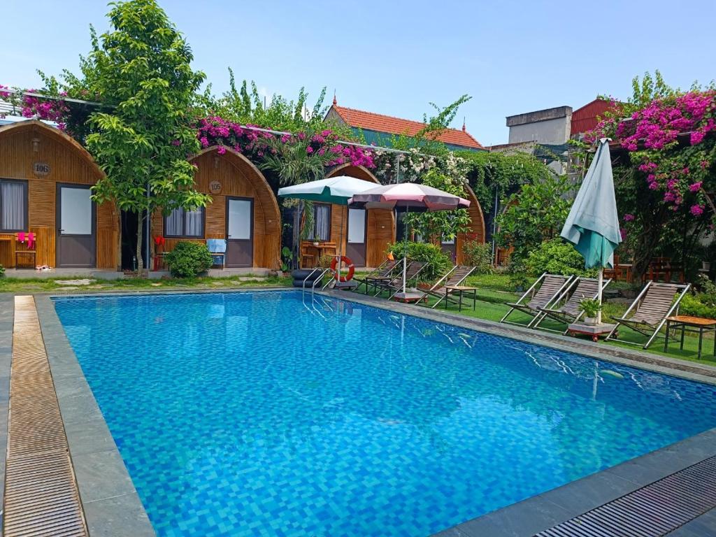 a swimming pool with chairs and umbrellas next to a house at Tam Coc Village Bungalow in Ninh Binh