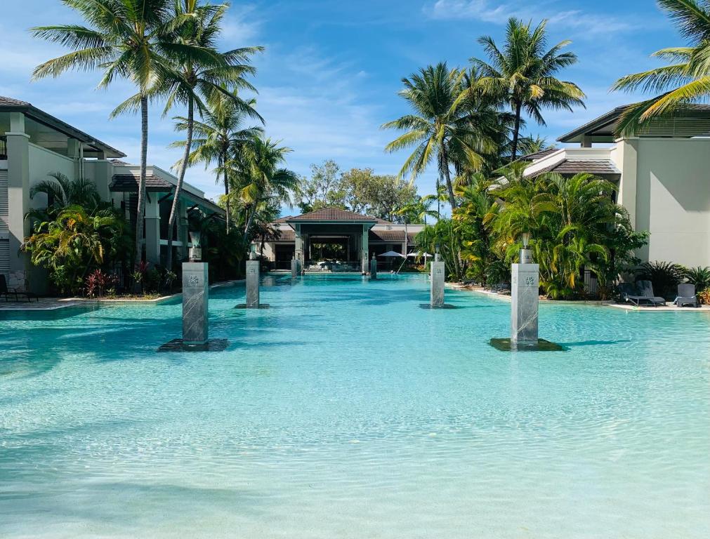 a swimming pool with palm trees and blue water at Tropical Retreat - Poolside Swimout - Ground Floor - Sea Temple Resort & Spa Port Douglas in Port Douglas